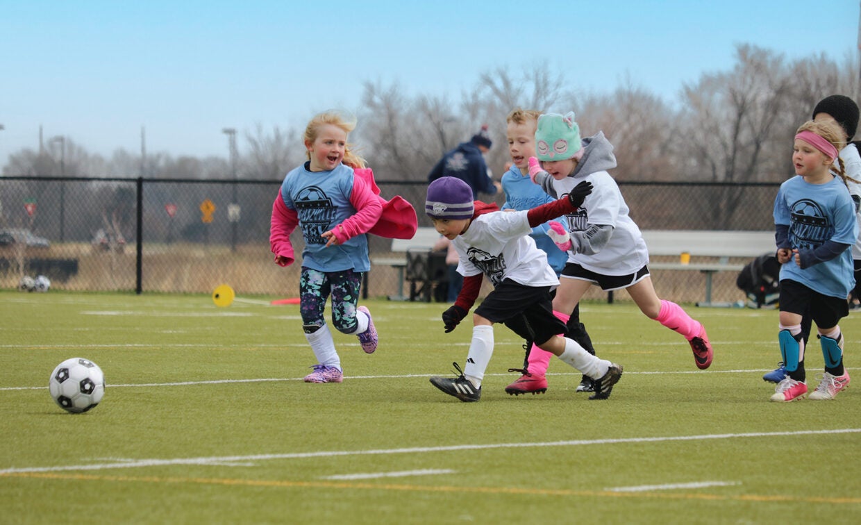 three girls and two boys play soccer outside on a field.