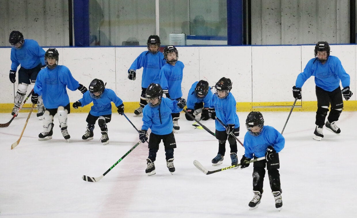 Boys in hockey gear practice skating on the ice with their sticks.