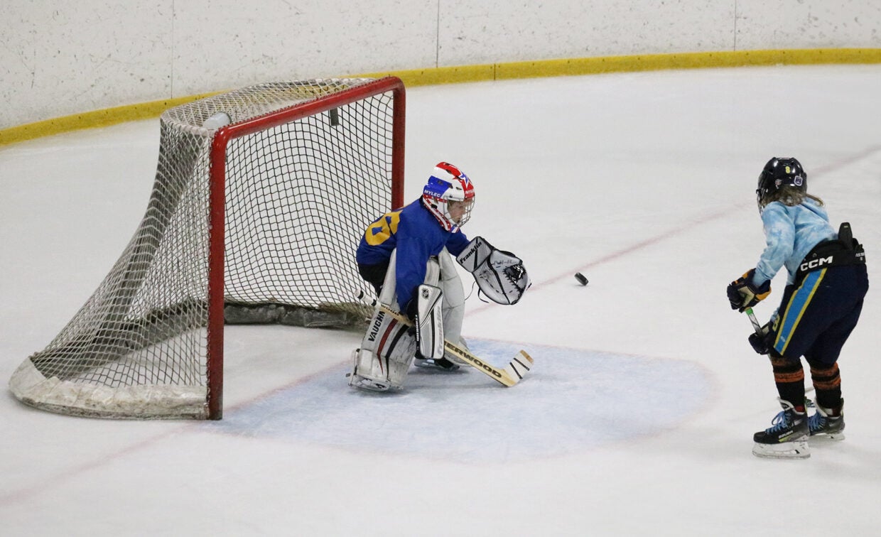 A boy in hockey gear attempts to shoot a goal against a goalie also in hockey gear on the ice.