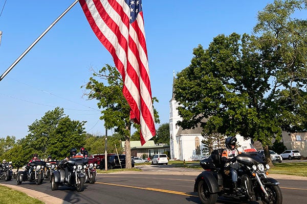 Motorcyclists driving past the American flag