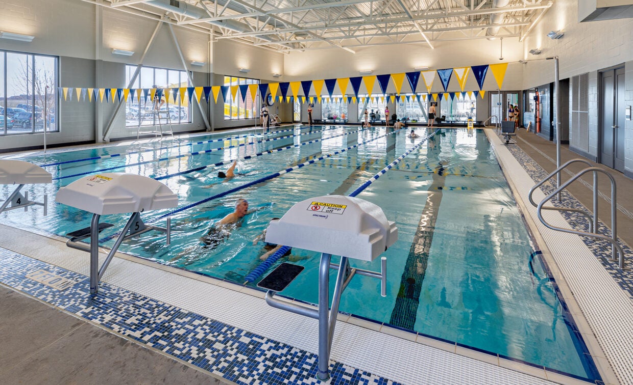 alt= Adults swim laps in a lap pool with six lanes.