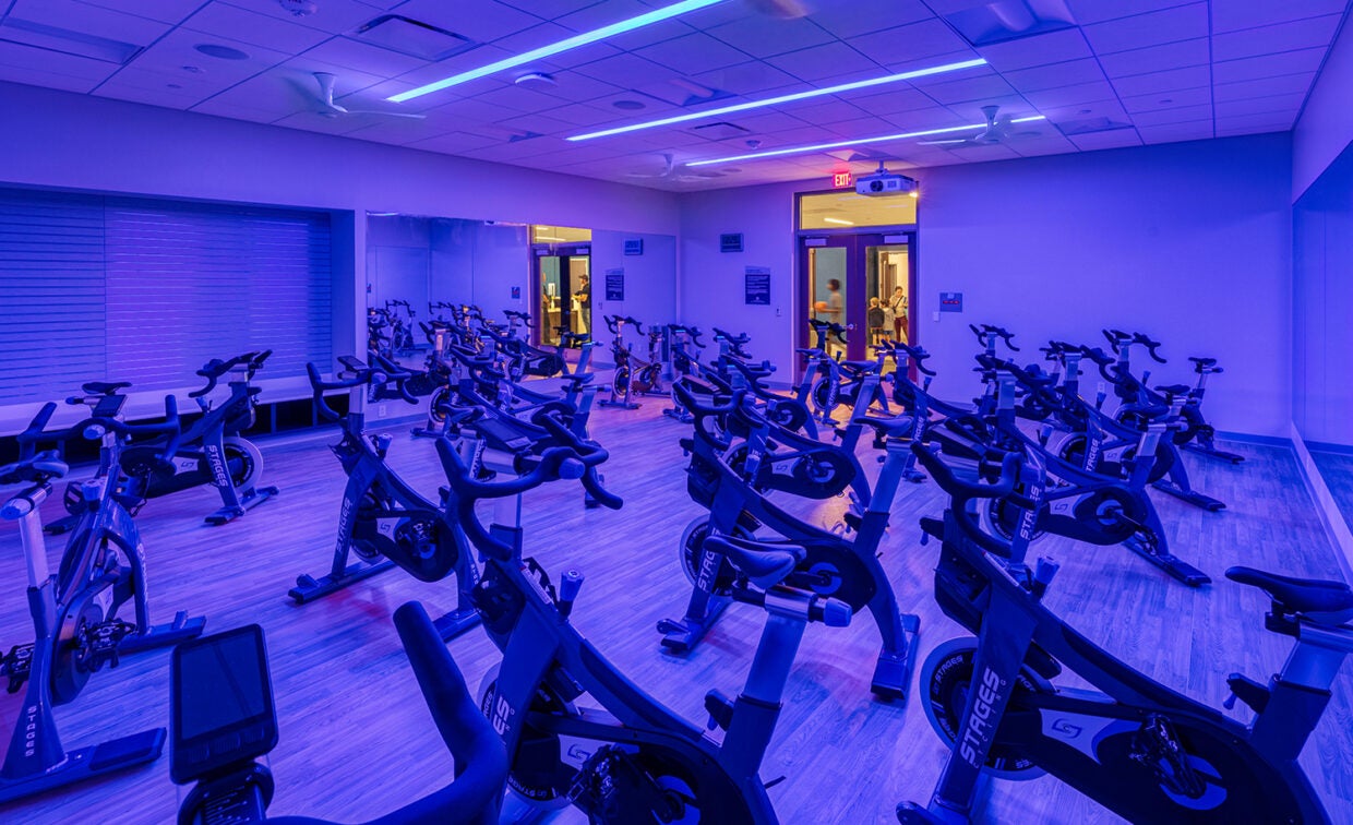 alt= Stationary bikes in a room with purple lighting.
