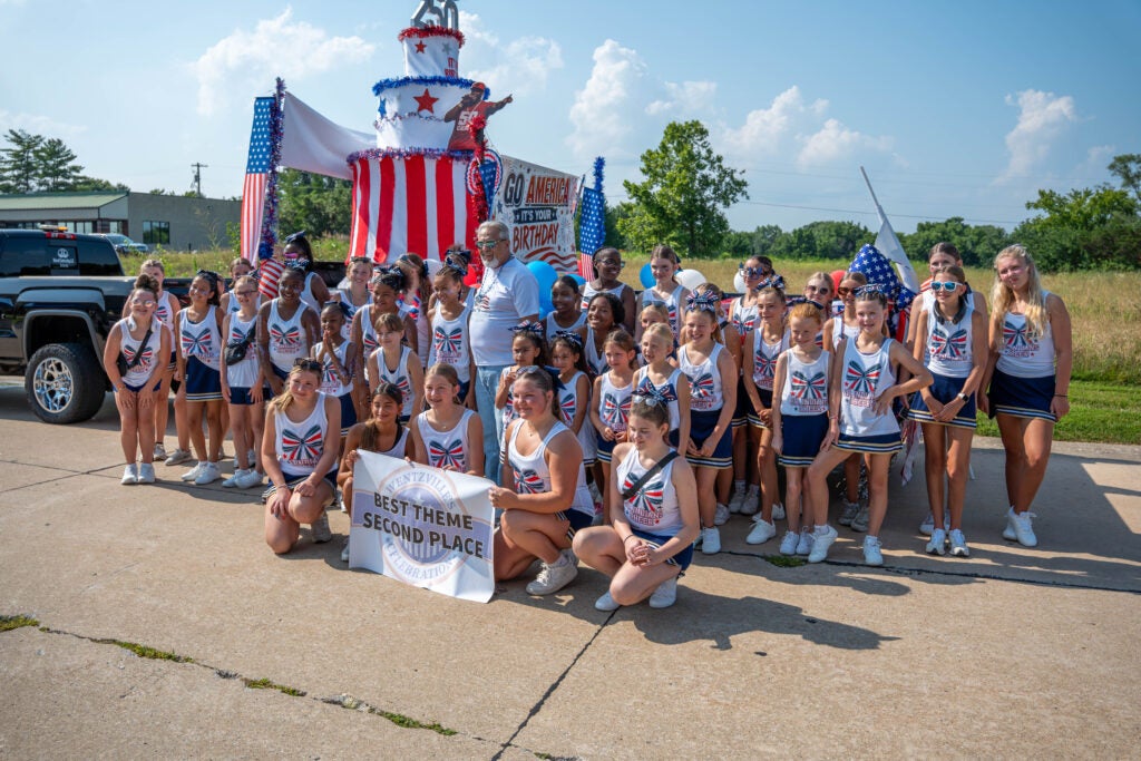 Group of people holding a banner, in front of their parade float with the mayor