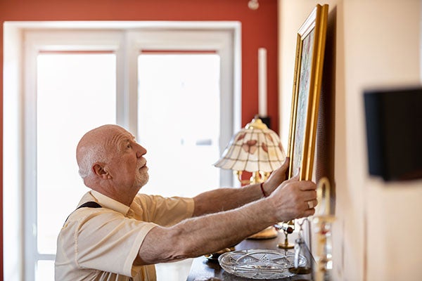 An elderly man putting up a frame on a wall
