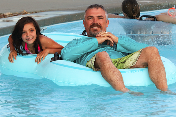 alt= A young girl and man float on a double innertube in the pool.