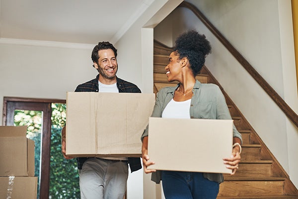 Couple homeowners moving in, carrying boxes and unpacking in new purchased home as real estate investors. Smiling, happy and cheerful interracial man and woman, first time buyers and property owners.