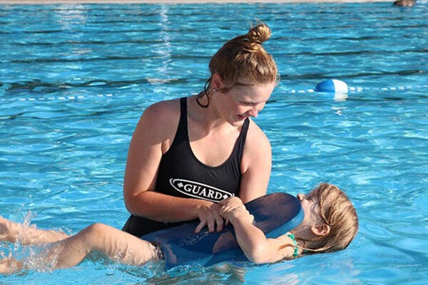 A swim instructor helps a child with a kickboard in the pool