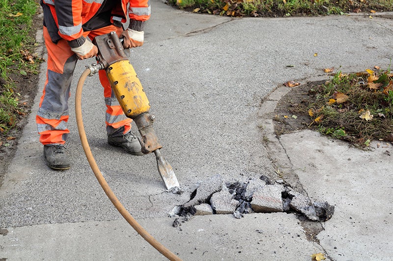A man uses a machine to bore into the asphalt