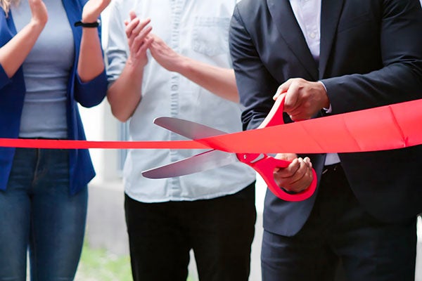 man cutting a ribbon with people in the back clapping