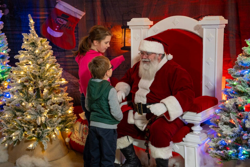 Santa in chair talking to two children.