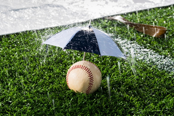 alt= A baseball sits on a rainy field under a tiny umbrella.