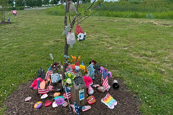 alt= A tree with painted rocks, American flags and other colorful decorations at it's base.