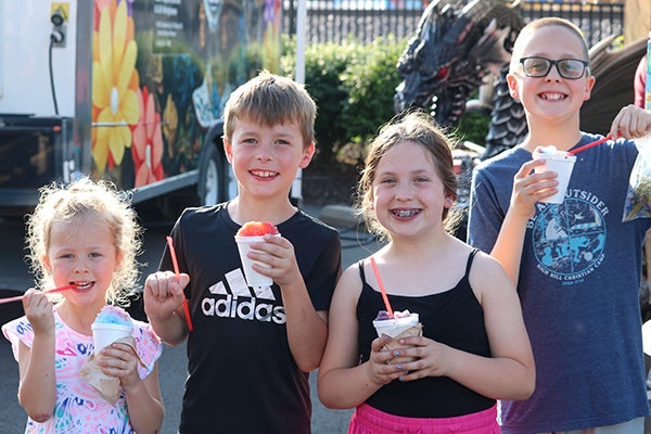 alt= Two girls and two boys smile and eat snow cones.