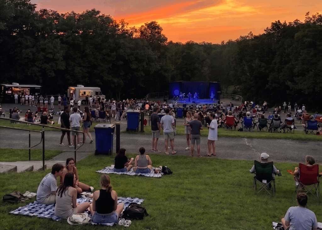 crowd of people facing an outdoor stage watching a concert at sunset