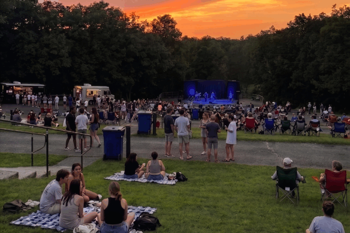 crowd of people facing an outdoor stage watching a concert at sunset