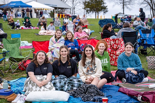A group of girls sit in chairs on blankets on the lawn.