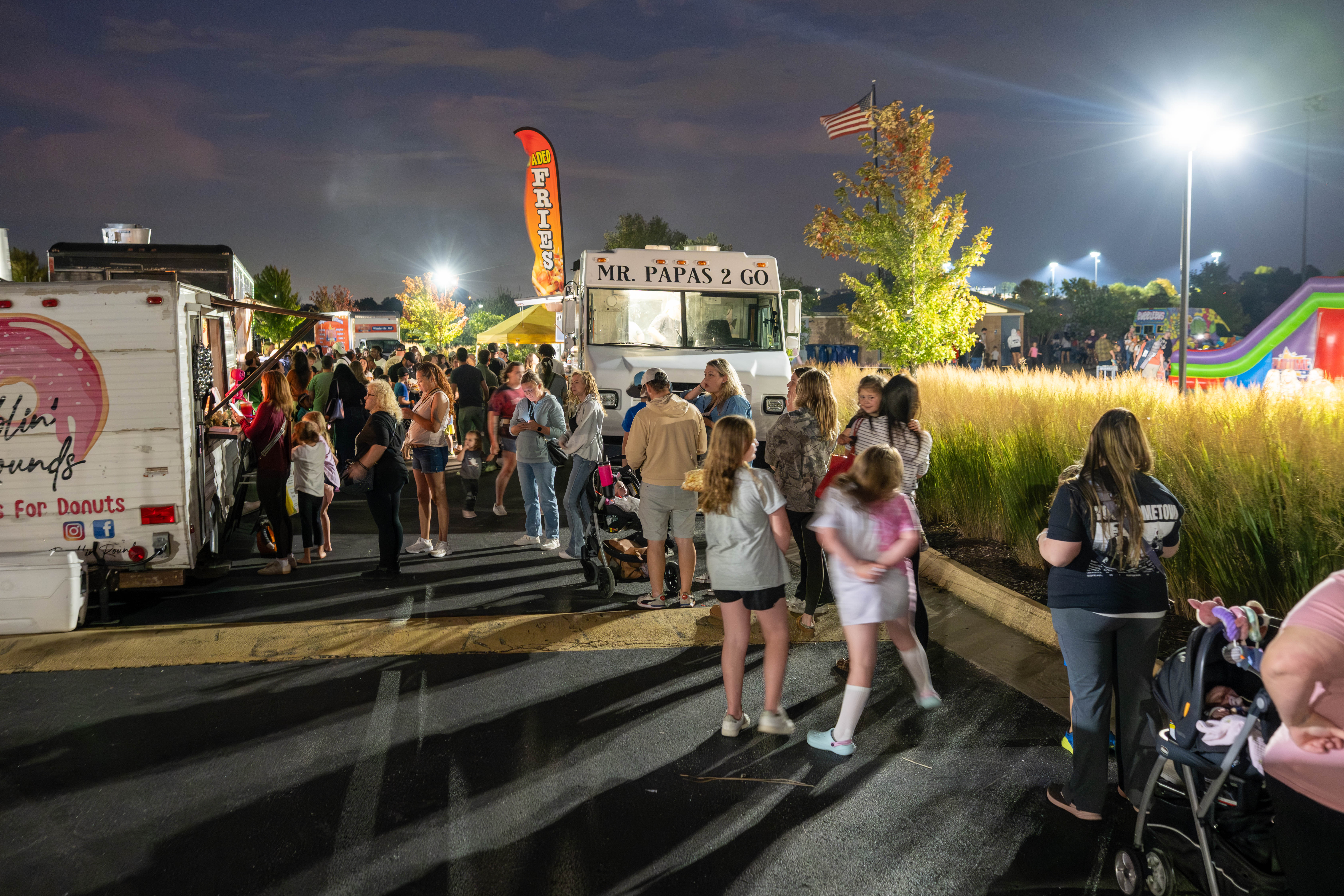 a crowd of people sitting on blankets and lawn chairs in a field facing an outdoor movie screen