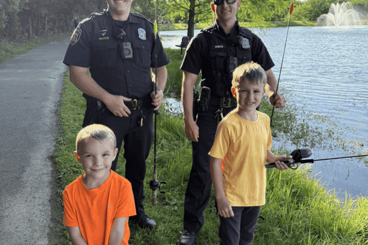Police officers and kids standing in front of a lake.