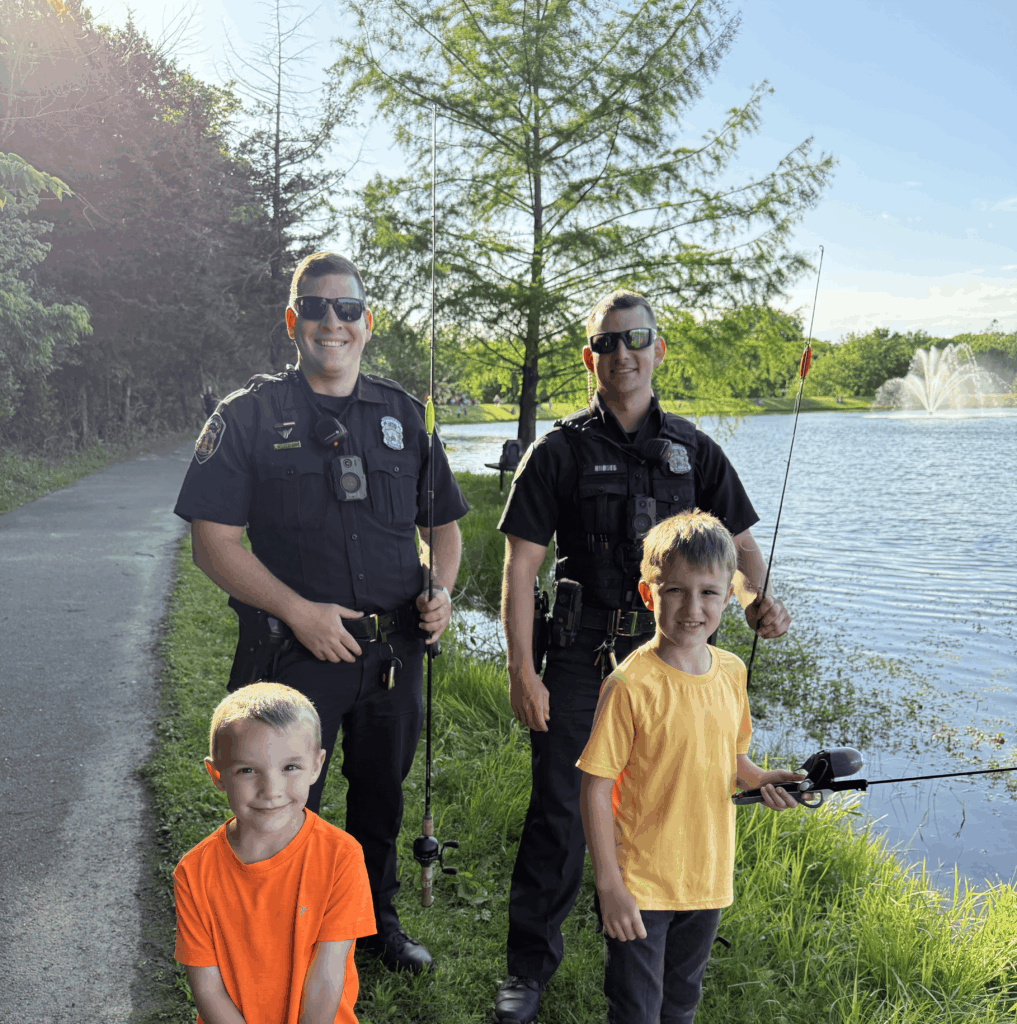 Police officers and kids standing in front of a lake.