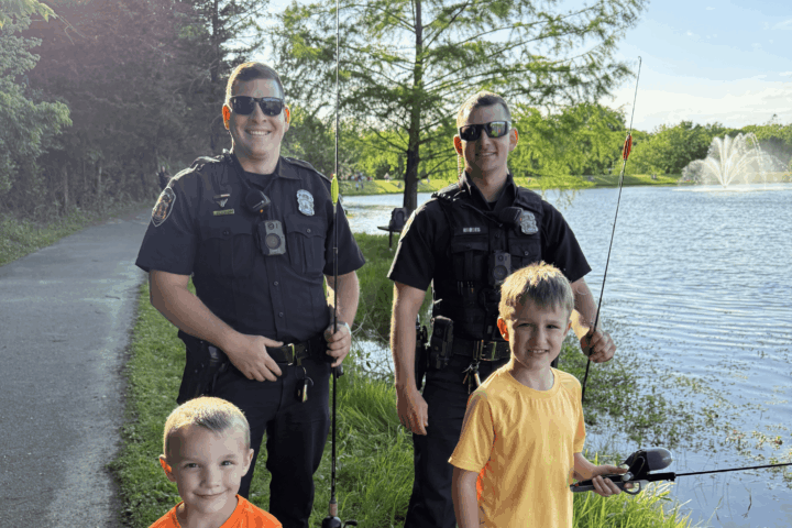 Police officers and kids standing in front of a lake.