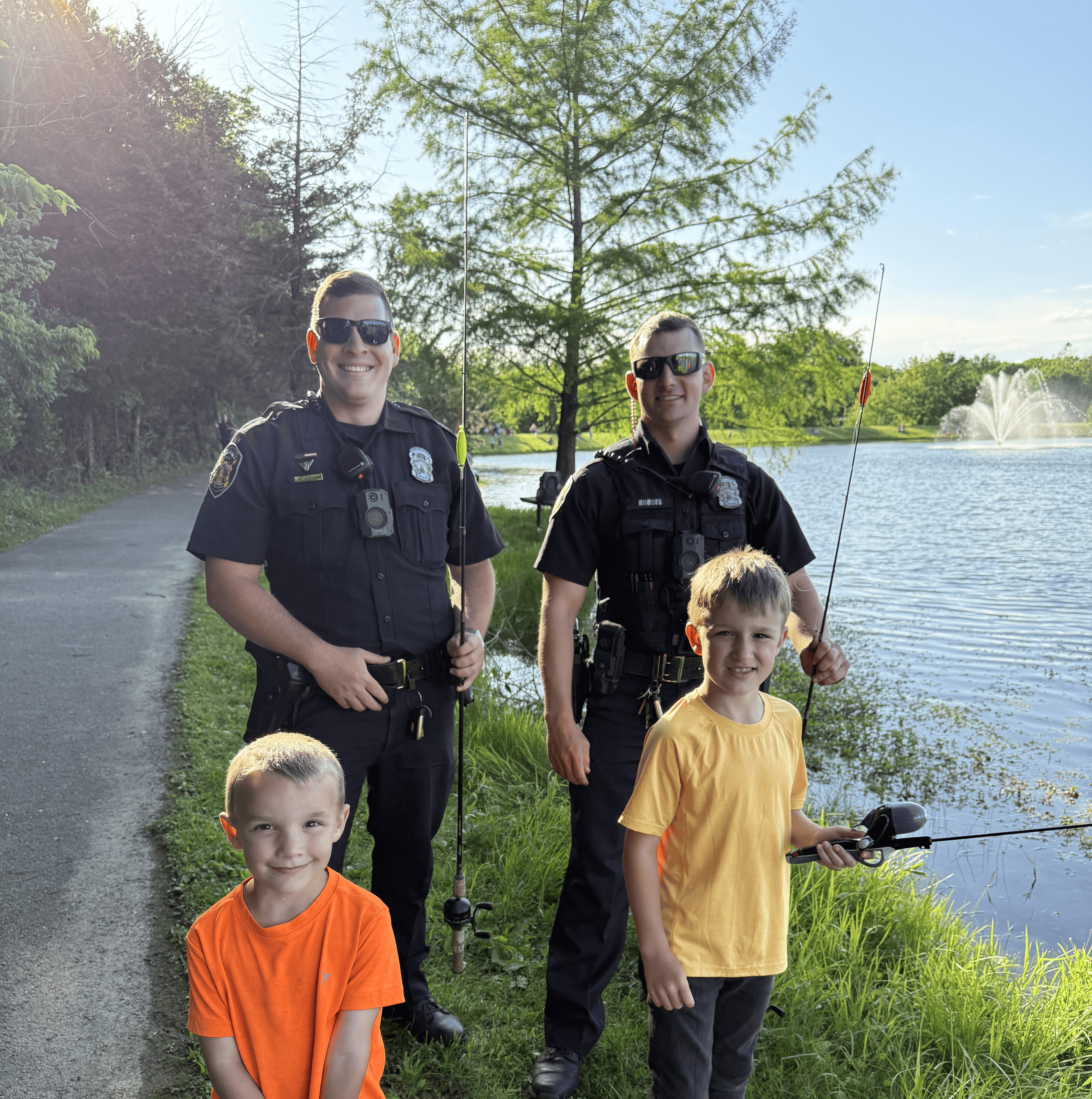 Police officers and kids standing in front of a lake.