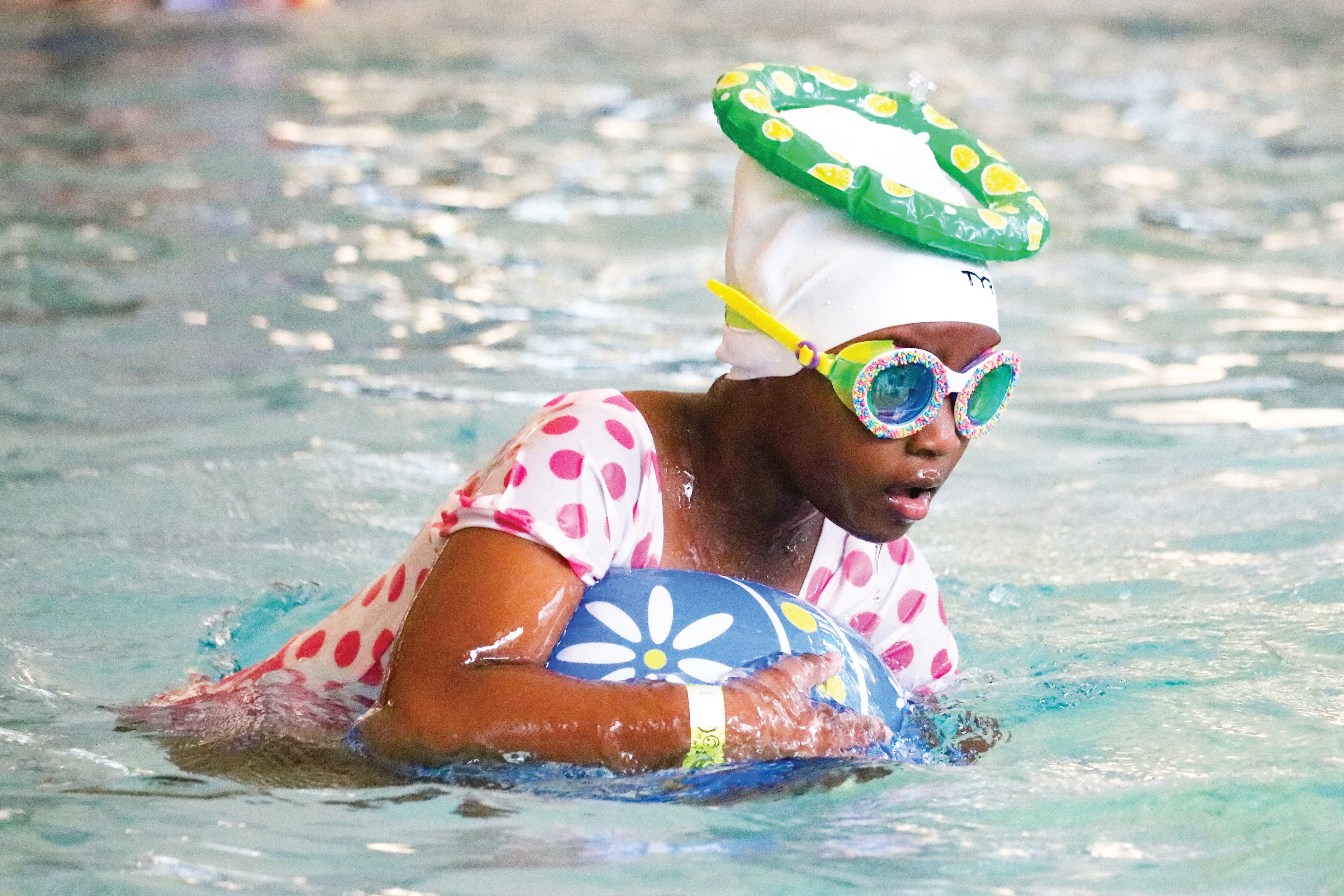 Girl swimming in pool with inflatable eggs, swim cap and goggles