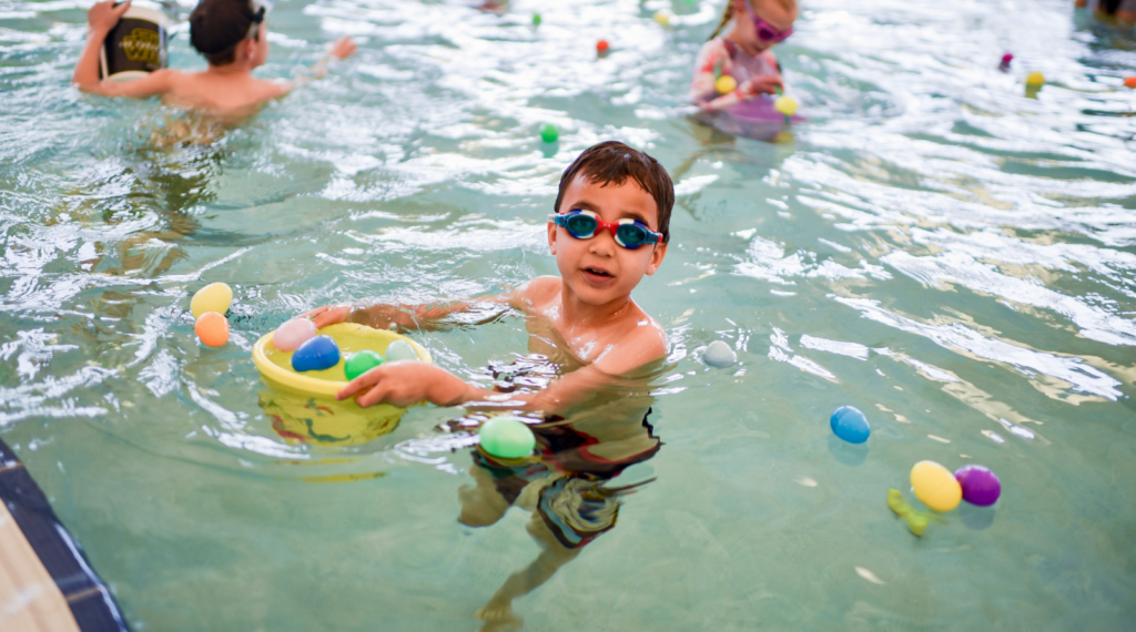 boy in pool smiling. plastic easter eggs floating in water
