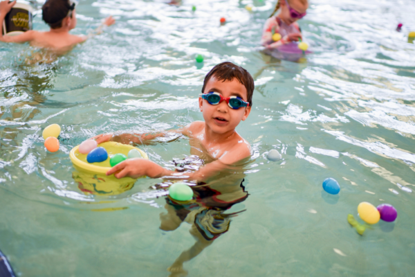 boy in pool smiling. plastic easter eggs floating in water