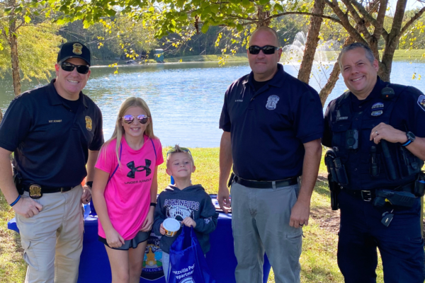 Police officers and kids standing in front of a lake.