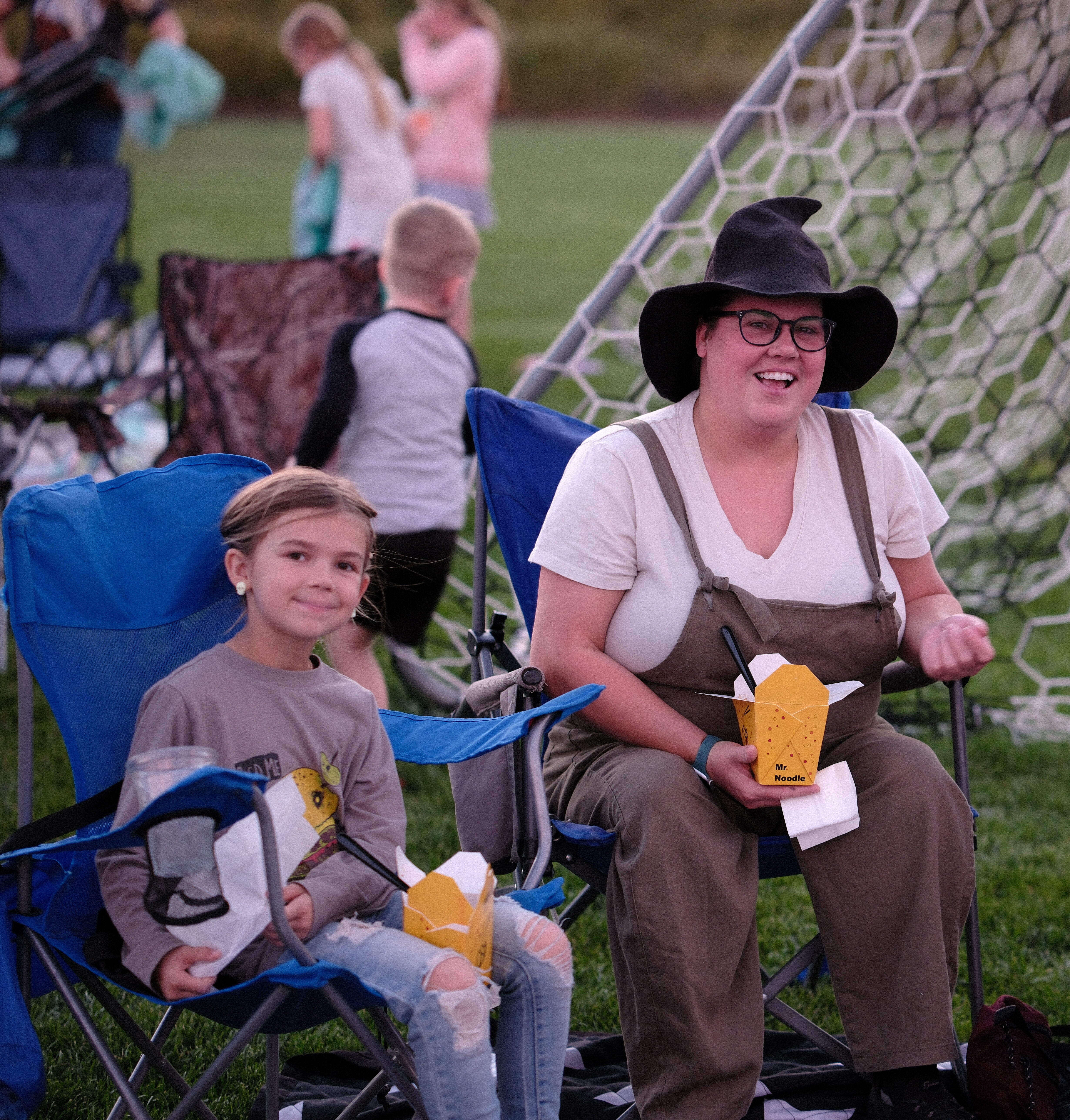 three people sitting in lawn chairs eating snacks on a soccer field