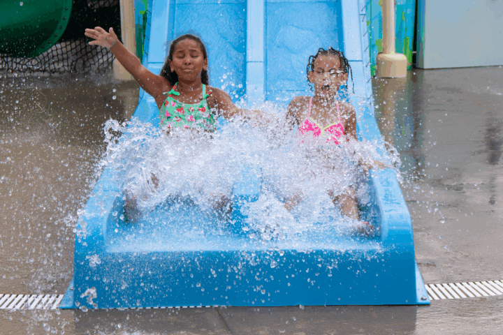 two girls holding hands going down the slide at the pool