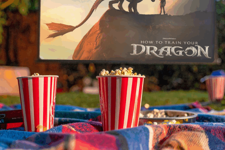 Two buckets of popcorn on a blanket in front of an outdoor movie screen