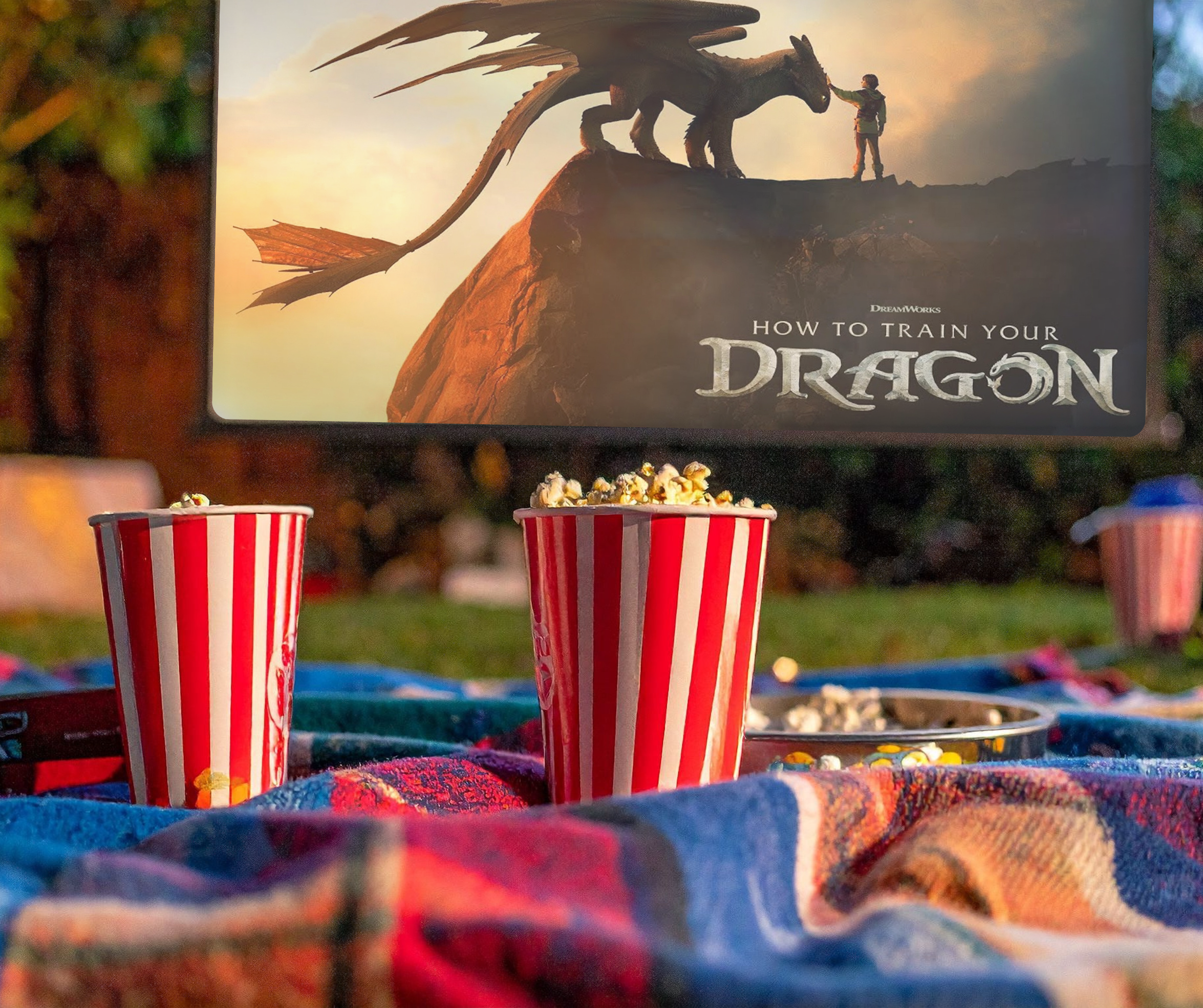 Two buckets of popcorn on a blanket in front of an outdoor movie screen