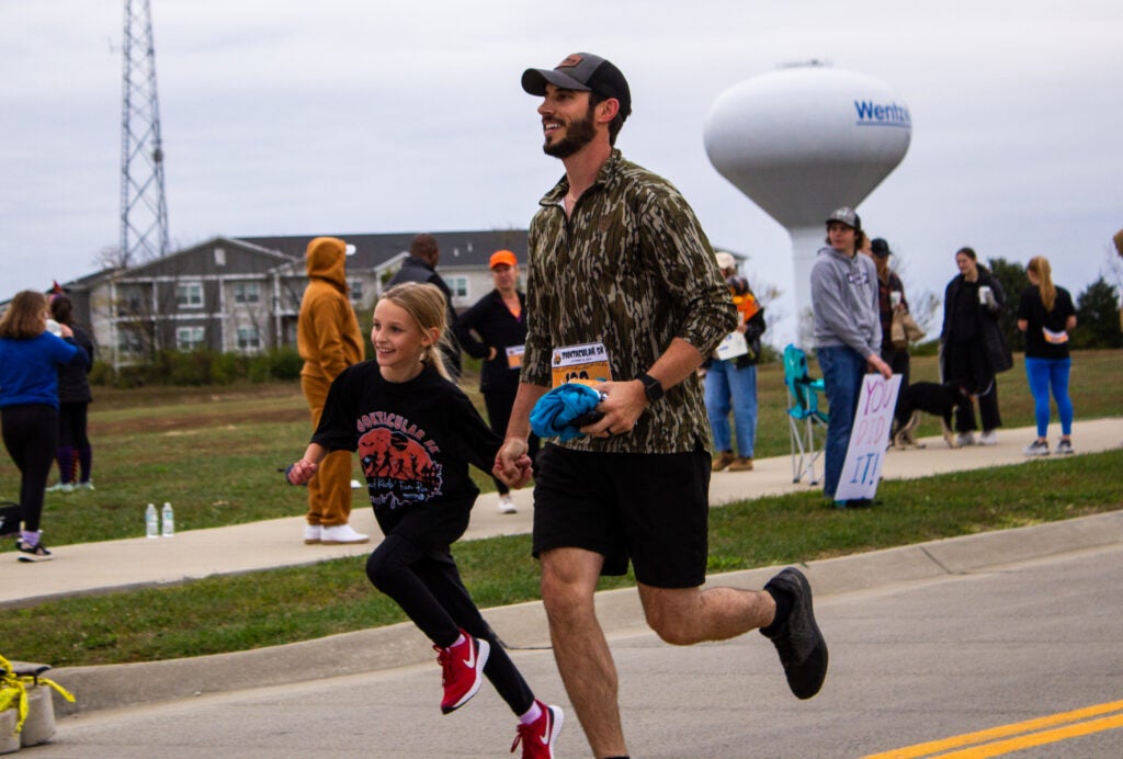 dad and daughter smiling while running towards the finish line of a race