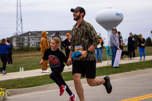 dad and daughter smiling while running towards the finish line of a race