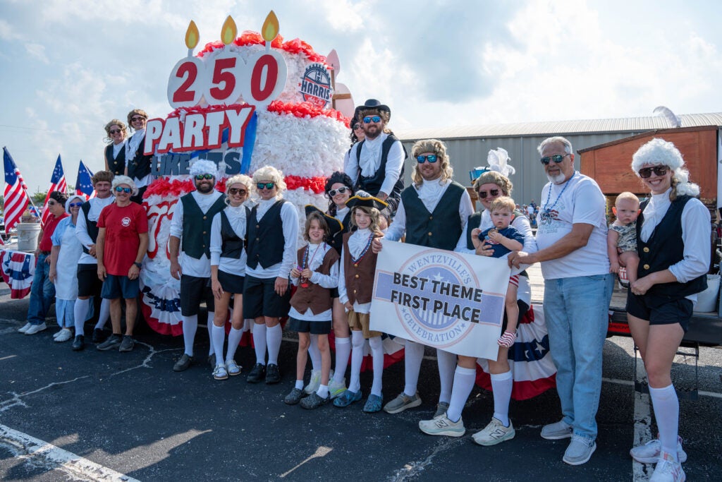 Group of people holding a banner, in front of their parade float with the mayor